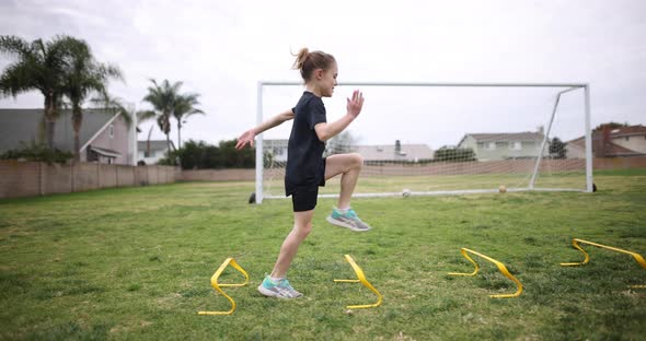A young athletic girl practices her running form over a set of speed hurdles. alt