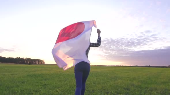 Young Positive Woman Runs Across the Field at Sunset with the Flag of Japan Slow Mo alt