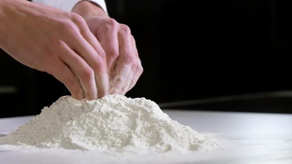 cook makes slide of white wheat flour with his hands to start making dough alt