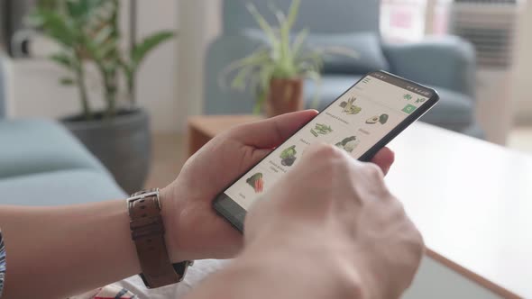 Hands Using Smartphone Buys In Internet Shop. Male Selects Vegetables In Grocery Online Store alt