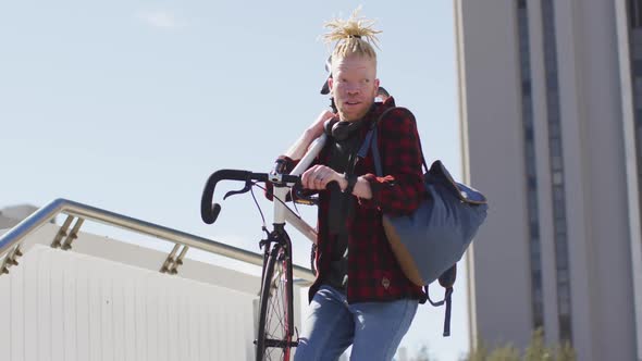 Thoughtful albino african american man with dreadlocks going down stairs with bike alt