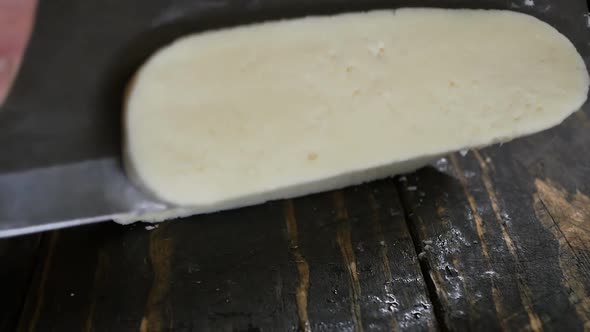 Cook's Hands Cut Soft Cheese with a Large Knife on a Wooden Brown Table