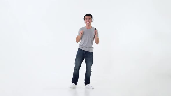 Asian man wearing headphones enjoying listening to music online from smartphone and dancing
