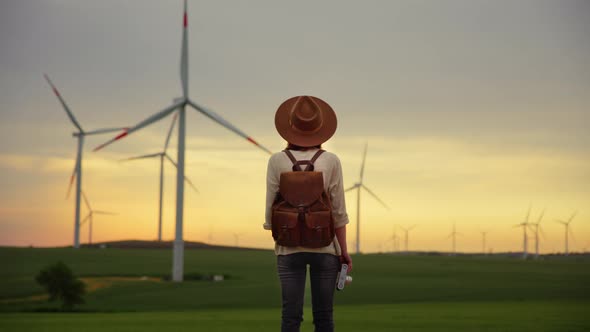 Attractive photographer with retro camera looking at windmills in field alt
