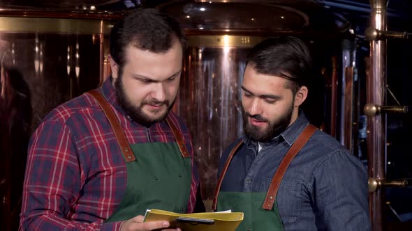 Two Beer Makers Smiling To the Camera, While Working at Their Brewery alt