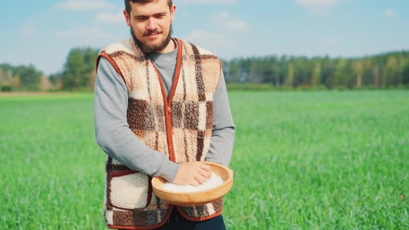 A Young Peasant Man Is Sowing the Field with Grain at a Village. A Farm Concept. alt