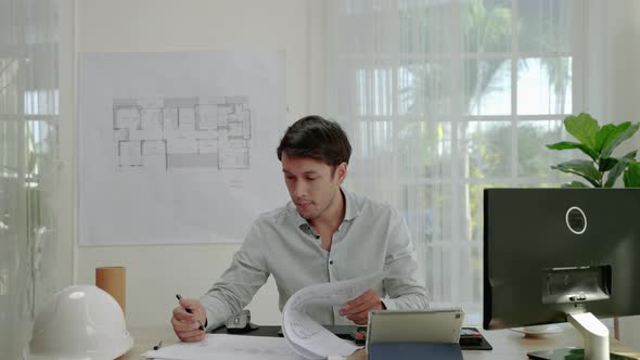 male architect or engineer is busy with his work on a desk full of house blueprints and computers