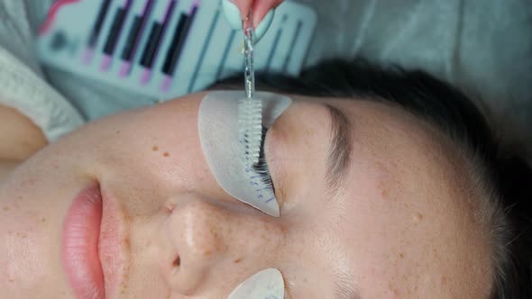 Eyelash Extension Master Combs the Extended Eyelashes on the Eye of a Beautiful Woman with a Brush alt