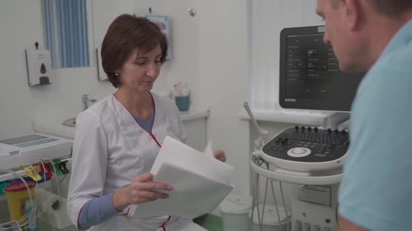 Female Doctor Consults Male Patient Holding Test Results in Hands in Office of Clinic alt