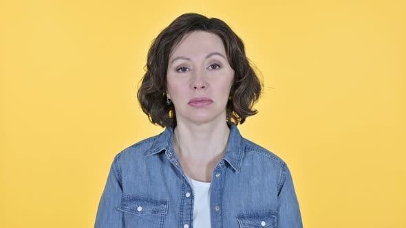 Sad Old Woman Looking at the Camera on Yellow Background  alt