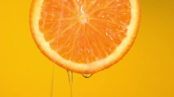 Natural oil flows down from orange on yellow background. Orange slice and water splashing, drops alt