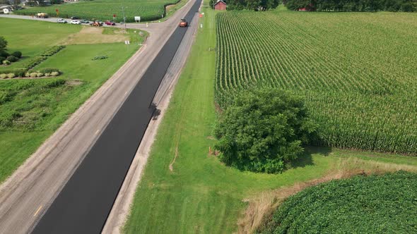 Drone view over rural highway being repaved in summer. Traffic waiting for crew for safety.