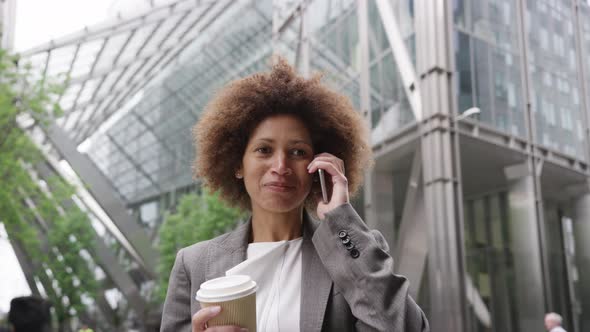 Afro American businesswoman in city using smart phone with takeaway coffee