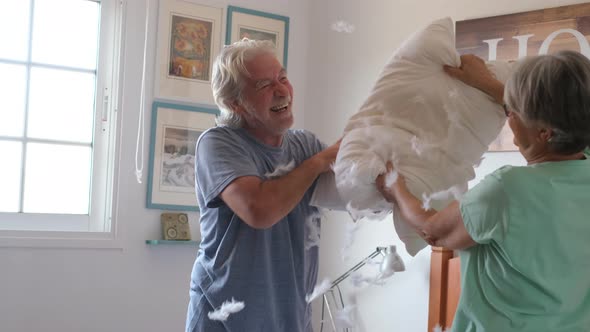 couple of two happy seniors having fun playing together on the bed at home fighting with pillows alt