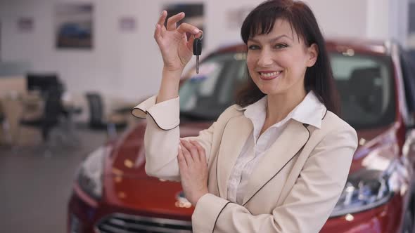 Portrait of Beautiful Caucasian Woman Posing with Car Key in Dealership Smiling Looking at Camera alt