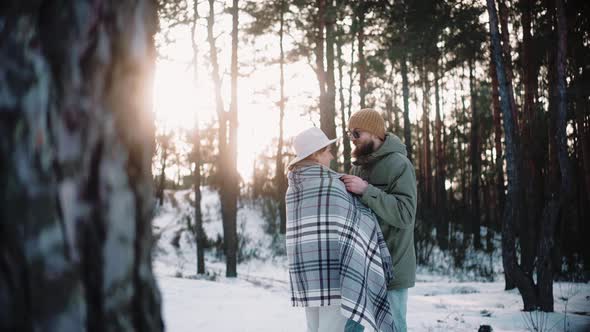 Man Hugs a Woman in Blanket in the Forest on a Winter Sunny Day Warming Her