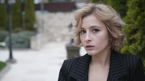 Portrait of Cute Serious Lady Looks at Camera with Light Smile Outdoors alt