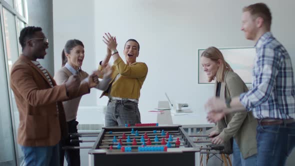 Young handsome casual multiethnic business people playing table football and relaxing at office