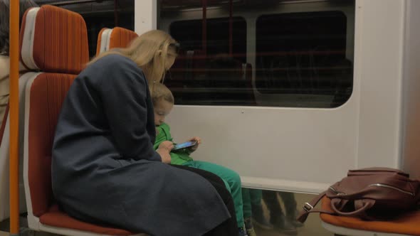 Mother and child using cell in moving subway train alt