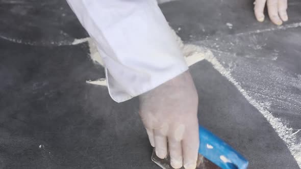Сhef collects flour from the table using a pastry scraper