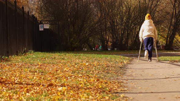 Kid Walks in Autumn Park on Crutches