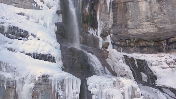 Waterfall in winter with icicles to the sides - close up sliding up alt