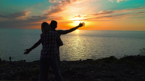 Couple of honeymoons stand at sunset and watch fading sun on horizon of sea alt
