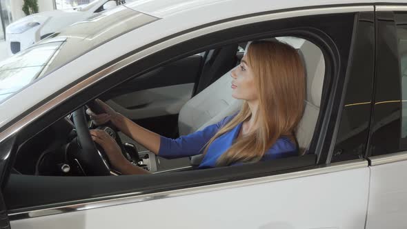 Beautiful Female Driver Smiling To the Camera Sitting in a New Car at the Dealership