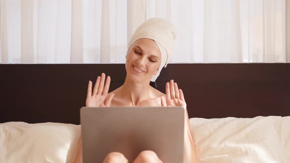 Young Woman in Bath Towel Resting on Cozy Bed and Using Wireless Laptop for alt