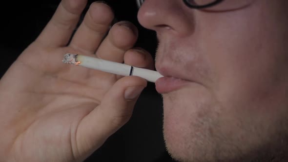 A Man Smokes a Cigarette and Exhales Smoke