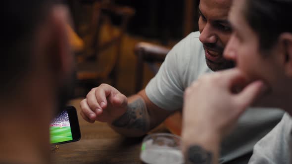 Three male friends watching football match on phone in the pub. Shot with RED helium camera in 8K. alt