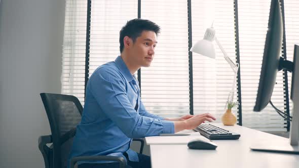 Asian attractive business man sitting on table using laptop computer and working in office workplace alt