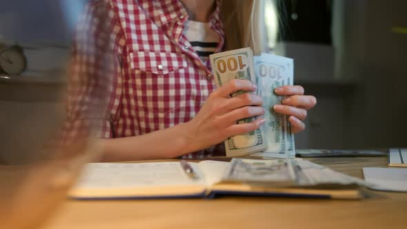 Woman Counting Cash at Working Desk. Attractive Blond Female in Checkered Shirt Sitting at Night in alt
