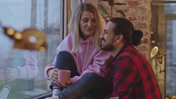 Portrait of Two Lovers Sitting Comfortably By the Window on a Rainy Evening alt
