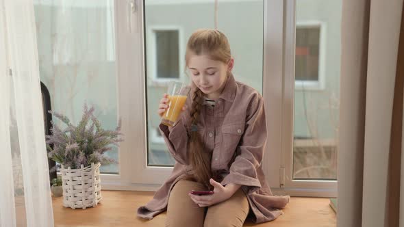 Girl Drinking Juice with a Phone in Her Hands alt