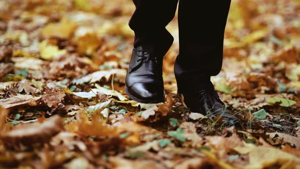 the legs of a stylish man walking through the autumn forest close-up