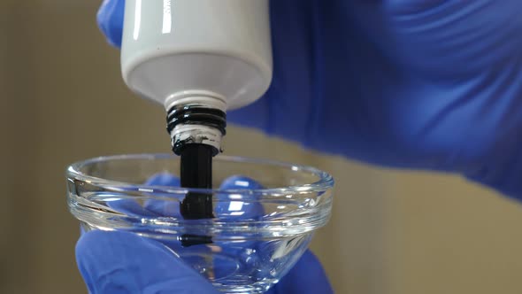 Beautician Squeezes Black Face Mask Into Glass Bowl for Subsequent Application To Face. Face alt