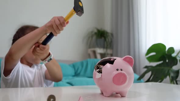 Little child girl is crashing piggy bank with hammer in slow motion
