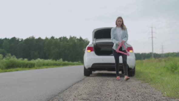 Stressed Woman Putting Emergency Sign on the Road. Woman Having Problems with Car, Stopped Her alt