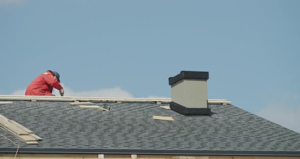 The Builder is Working on the Roof of the House  Laying Shingles alt