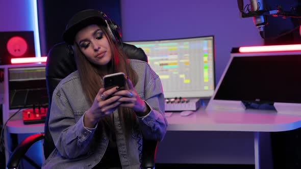 Musician Woman Sits in Chair in the Recording Studio and Uses Smartphone