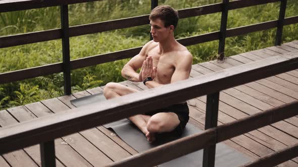 A calm half-naked guy with closed-eyes is doing meditation on the bridge alt