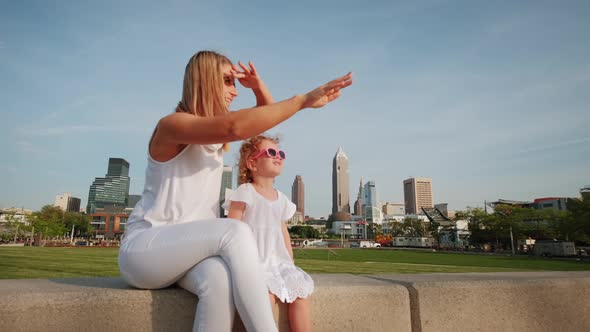 Happy Mother and Daughter are Resting in a City Park on a Bench alt