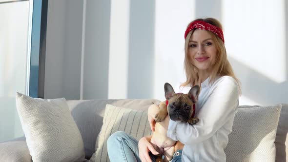 Young Woman in a White Shirt and Jeans Sits on the Sofa and Playing with Her Dog alt