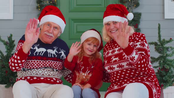 Senior Old Couple Grandparents with Grandchild Girl Kid Waves Hand Hello Hi Near Christmas House alt