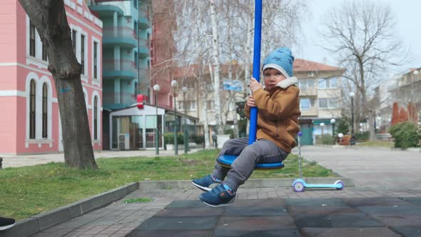 A Boy on a Playground in an Autumn Park Rides on a Swing in Cloudy Weather alt