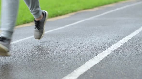 legs of a guy in sneakers running on a wet asphalt treadmill. Close-up alt