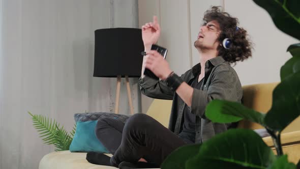 Curly Haired Young Man on the Couch Listening Music with Headphones alt