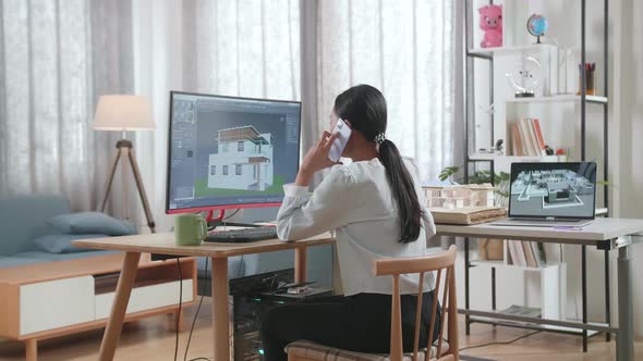 Asian Woman Engineer Talking On Smartphone While Designing House On A Desktop At Home alt