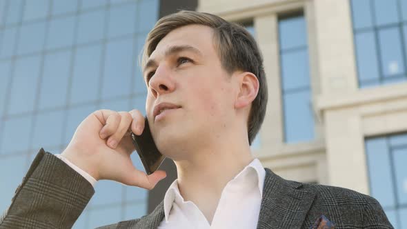 Portrait of Businessman Talking on Smartphone in Downtown Near Office Building